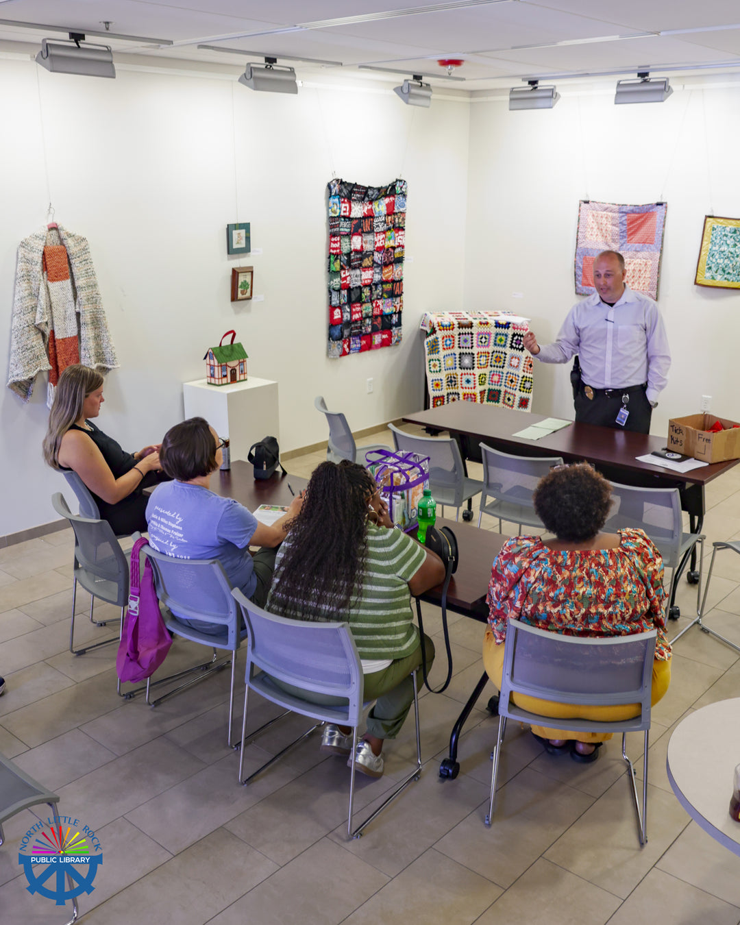 Four seated people listen to a presenter in a gallery with colorful art.
