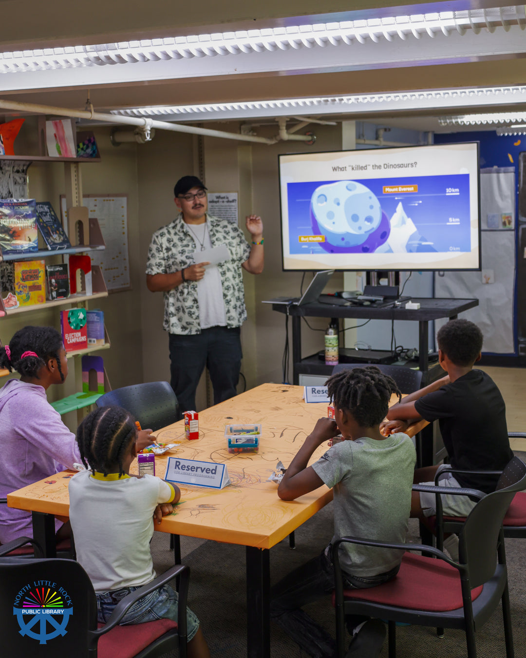 A paleontologist-in-training talks to a group of seated children about dinosaurs.