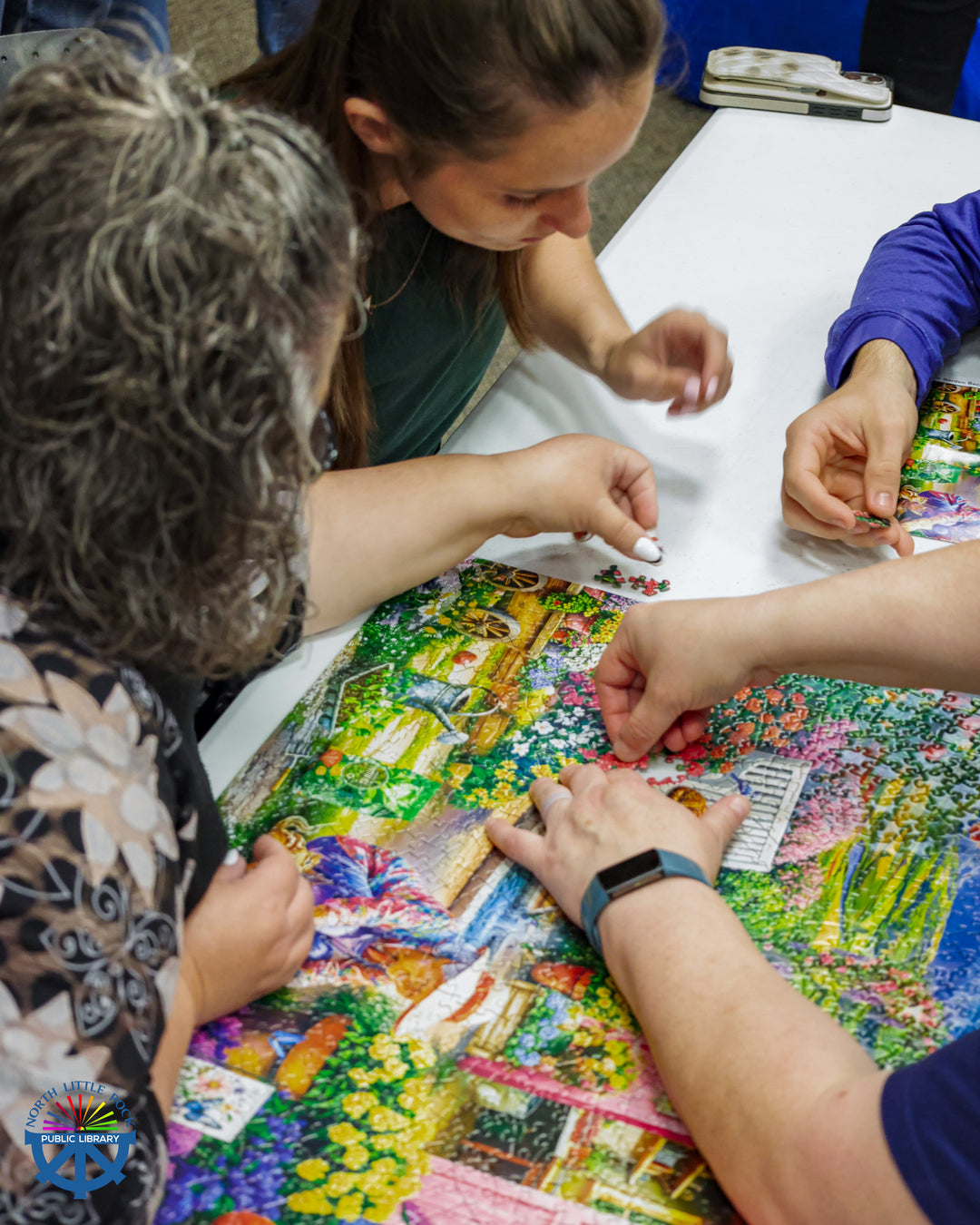 A close-up of a group of people working on a nearly-complete colorful puzzle.