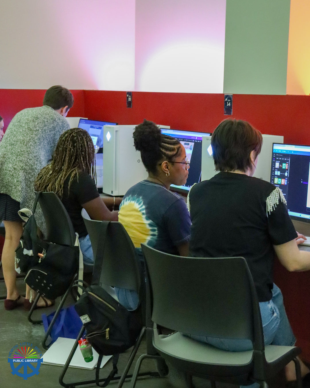 Library patrons sitting in front of computers getting assistance from staff members.