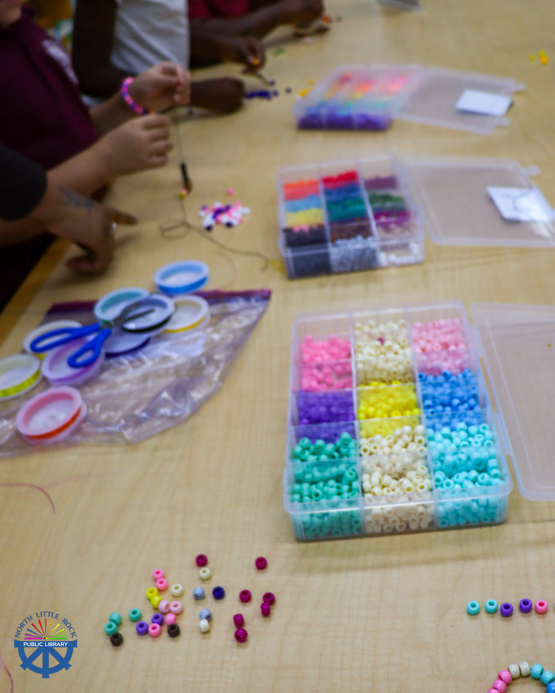 Tweens making bracelets with beads, cord, and scissors.