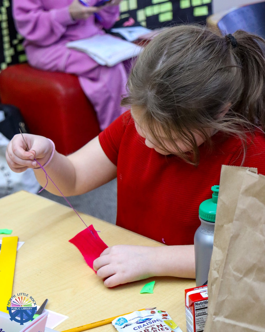 A tween uses purple thread to sew red felt.