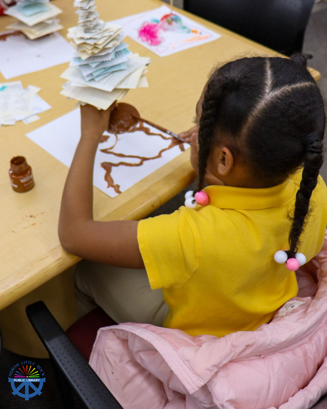 A tween paints the base of a paper tree.