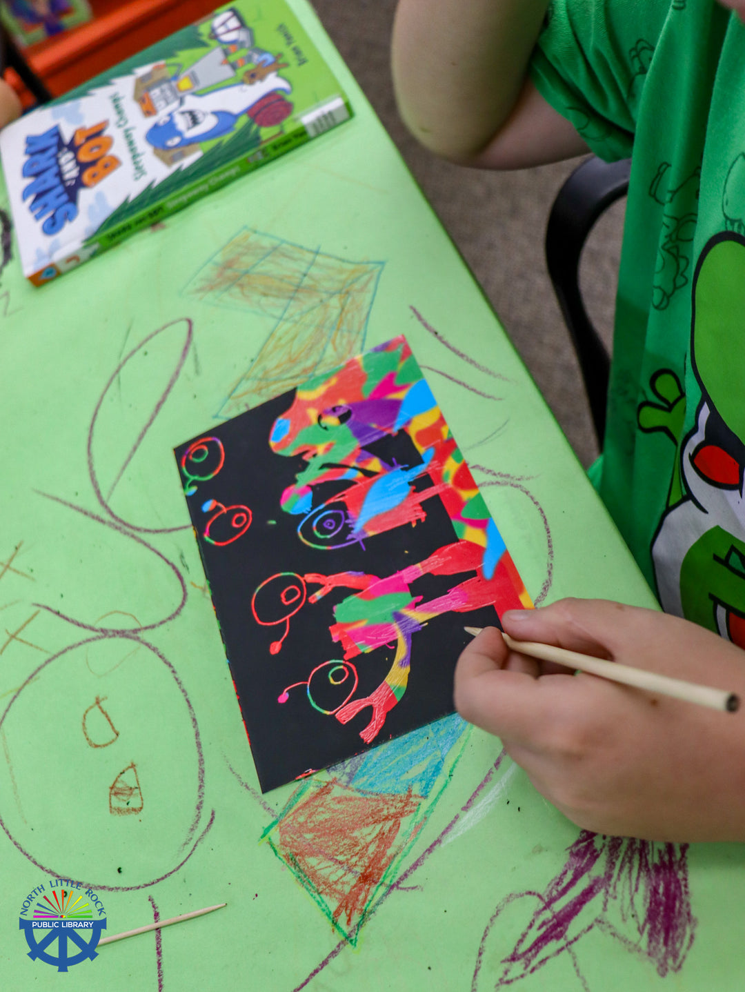 A tween scratches at a black piece of paper to reveal a colorful design.