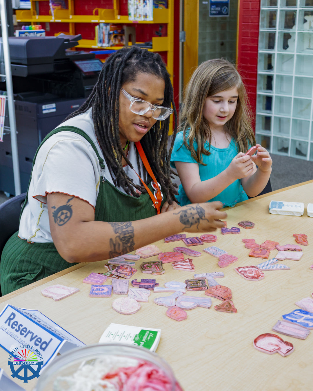 Tween specialist Drienne sit with a tween at a wooden table covered in pink stamps used for block printing.