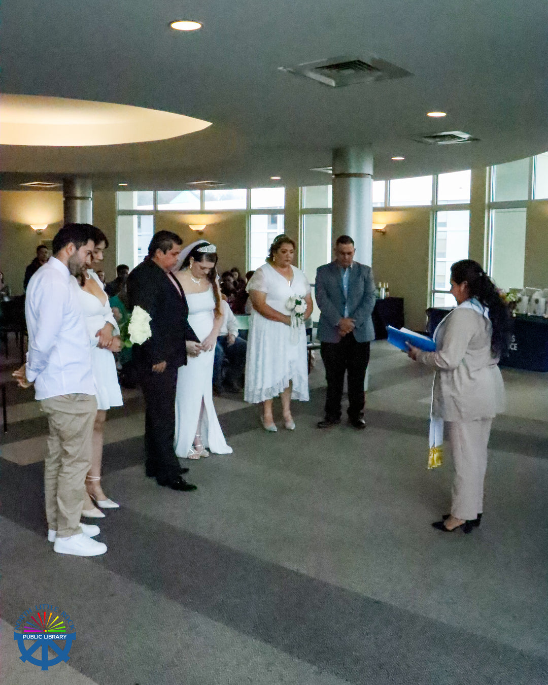 Three couples in wedding clothes stand in a semi-circle around an officiant 
