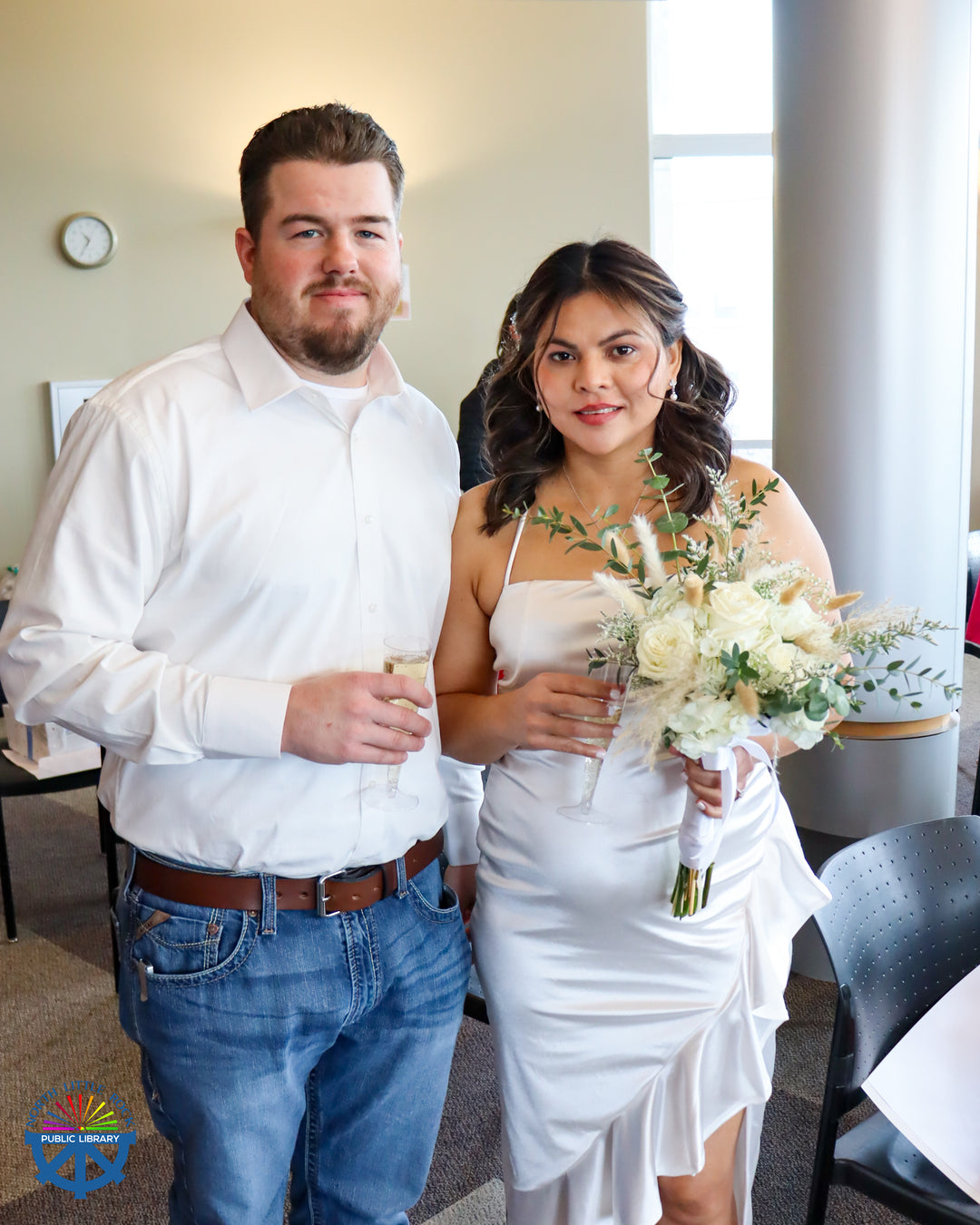 A woman in a white dress and bouquet poses for a picture with her new husband wearing a white shirt and jeans.