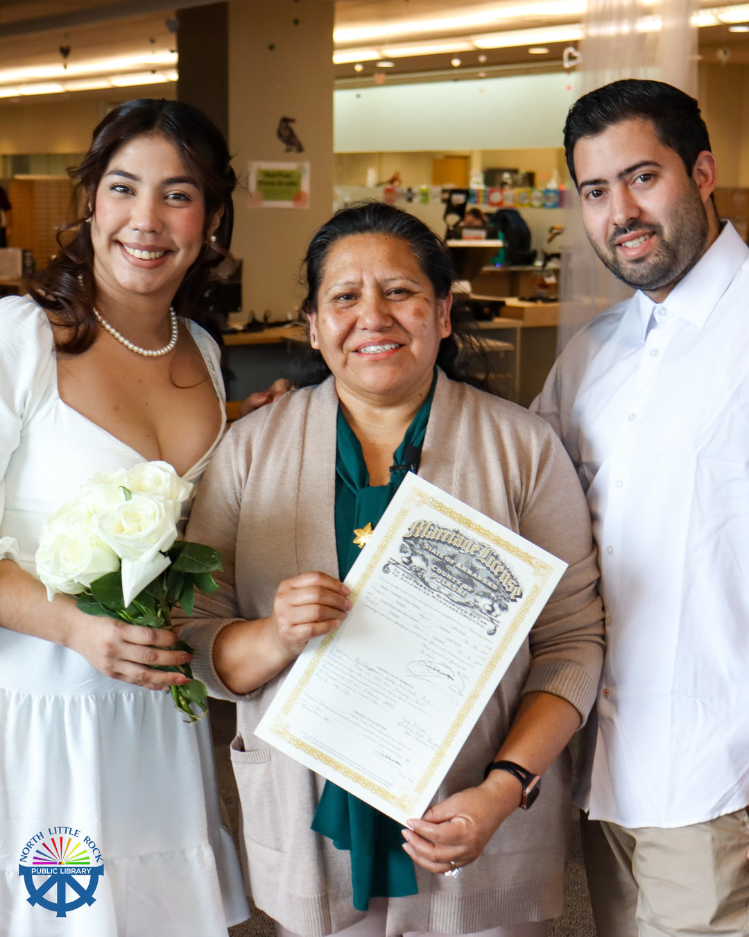 A newly married couple pose for a picture with their officiant, who holds their marriage certificate.