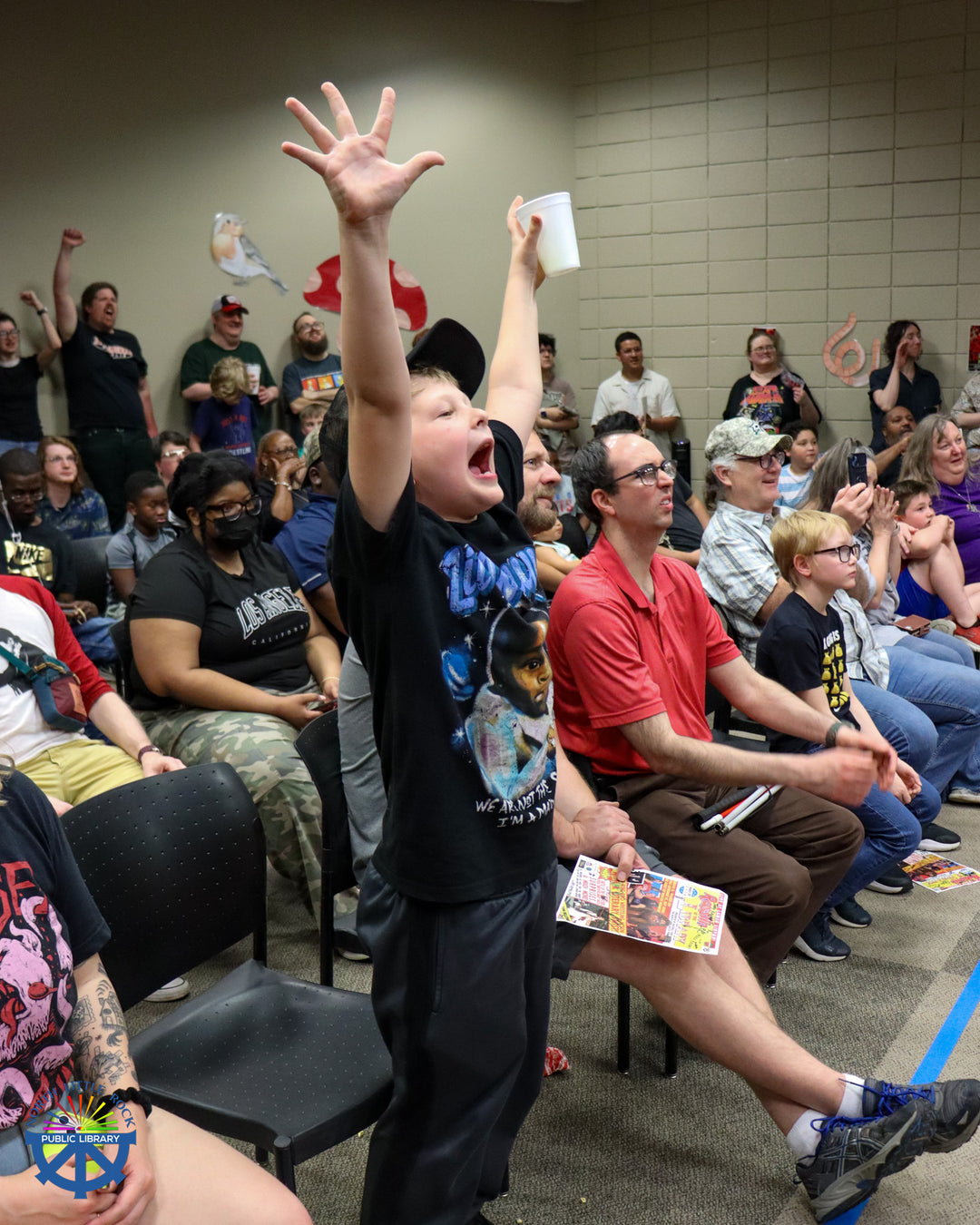 A child stands and cheers in a crowded room with people of all ages.
