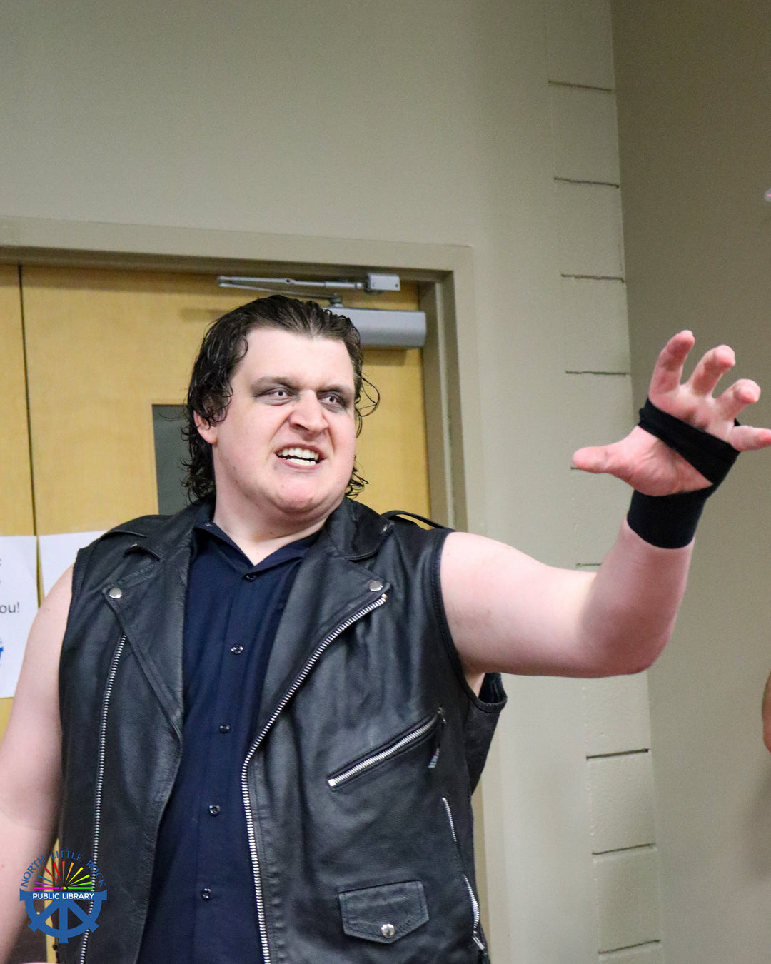 A tall wrestler with snake-like contact lenses enters the room menacingly, an arm outstretched.